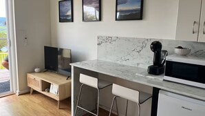 A modern kitchen with a marble countertop, a coffee maker, and a Hisense microwave. There are two bar stools and a television on a wooden cabinet.