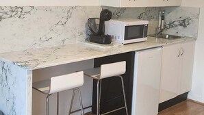 A modern kitchen with white cabinets, a marble countertop, a microwave, and two bar stools.