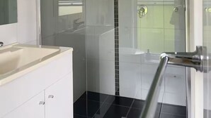 A modern bathroom with a glass-enclosed shower, a white sink, and a tiled floor.