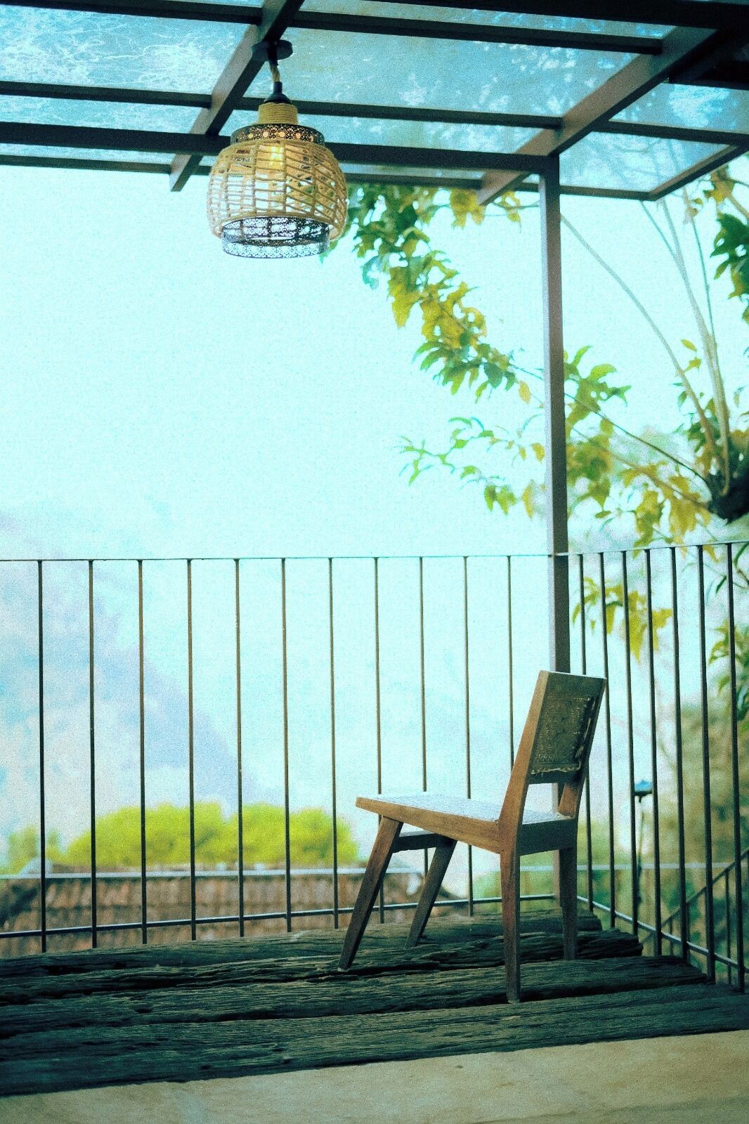 Un espacio de estar techado al aire libre con barandilla de metal, una lámpara colgante y una silla.