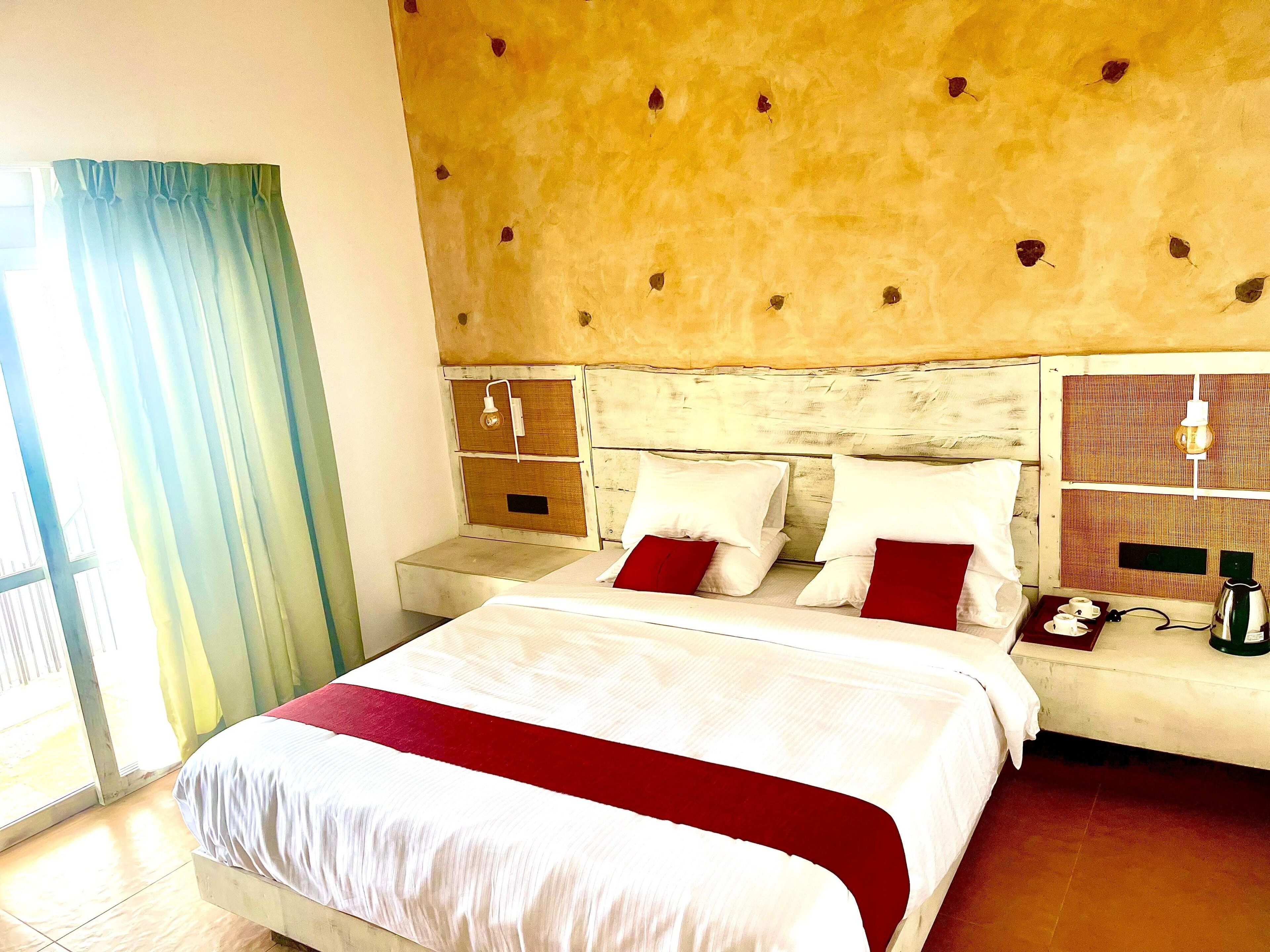 A hotel room with a bed, a nightstand, a lamp, and a window with curtains.