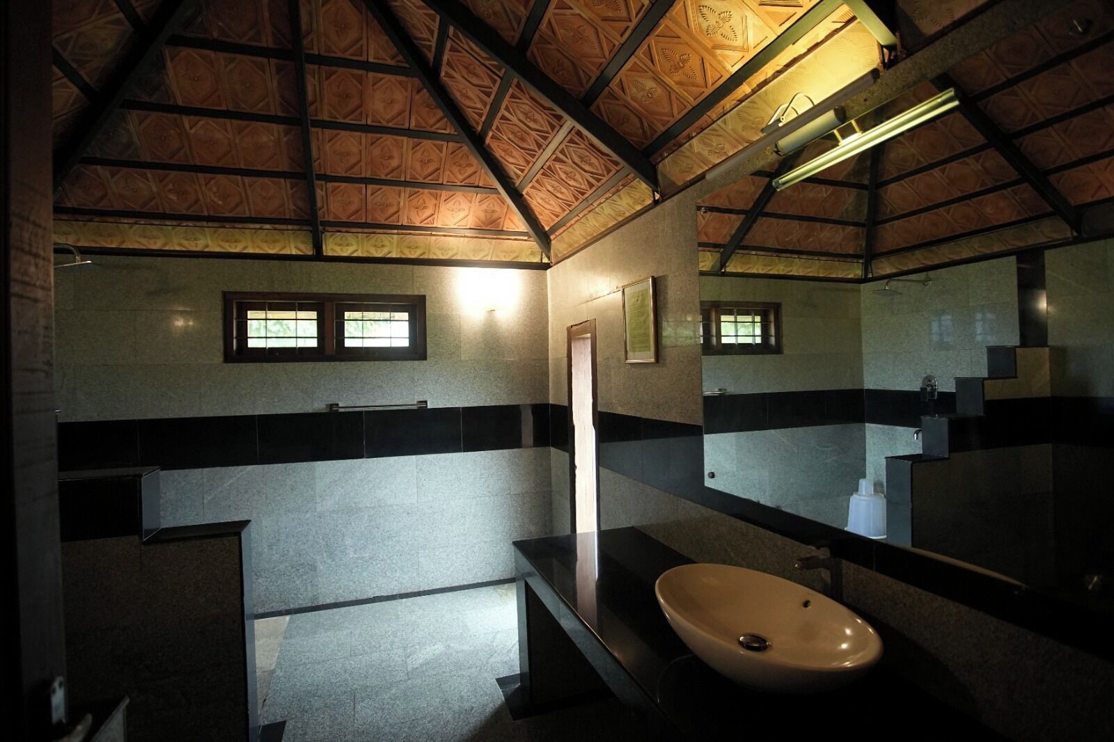 Une salle de bain avec un sol carrelé en pierre, un lavabo, un miroir et une fenêtre.