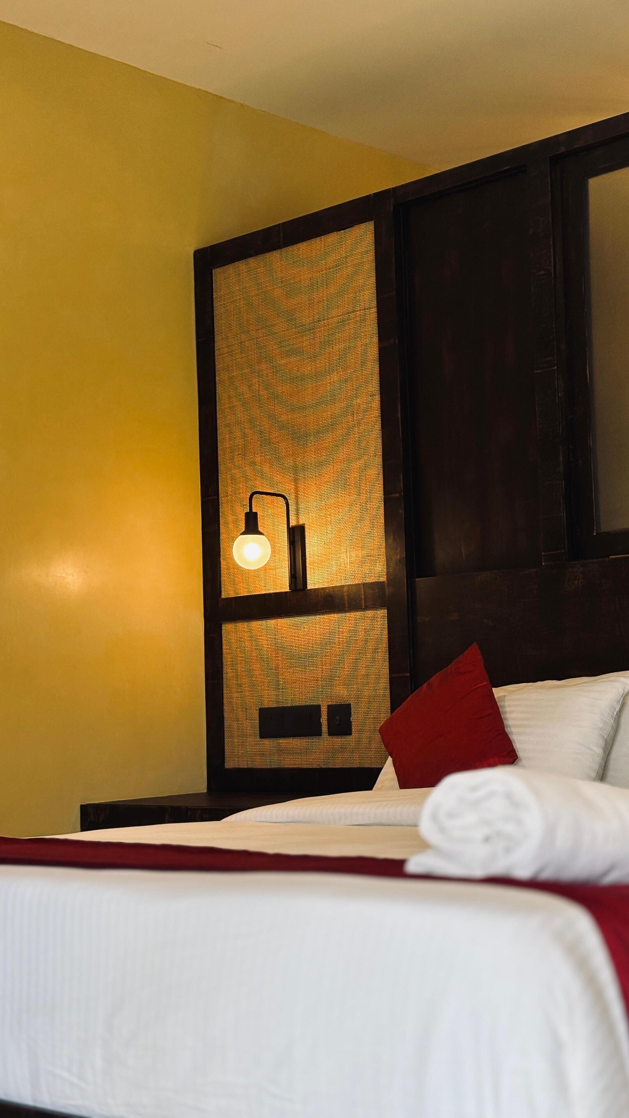 A hotel room with a bed, a wall-mounted lamp, and a large mirror.