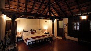 Una habitación con techo de madera, una cama con ropa blanca, dos mesitas de noche con lámparas y una silla de madera.