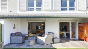 Ein zweistöckiges Haus mit überdachter Veranda, ausgestattet mit Korbmöbeln und einem Esstisch.