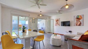 Ein modernes Wohnzimmer mit Essbereich, ausgestattet mit einer großen Glasschiebetür zu einem Außenbereich, einem Deckenventilator und einem wandmontierten Flachbildfernseher.