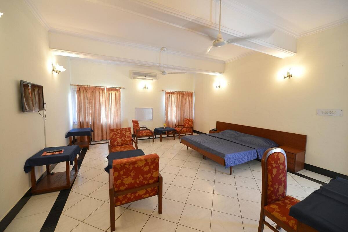 Une chambre d’hôtel comprenant un lit, deux chaises, une petite table, un bureau, un ventilateur de plafond et un téléviseur.