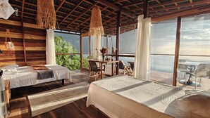 Una habitación con dos camas, una mesa de comedor y ventanas amplias que ofrecen vistas al exterior.