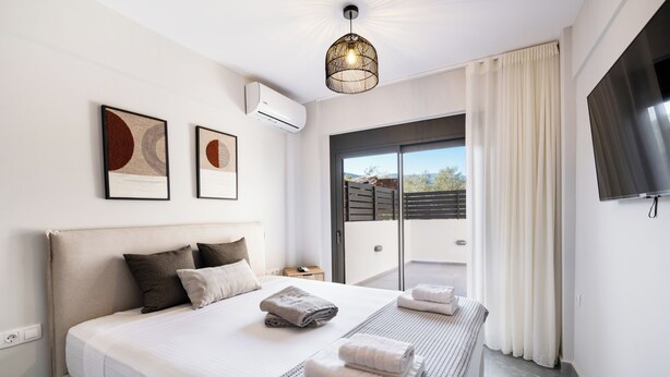 A modern hotel room with a large bed, a flat-screen TV, a balcony with curtains, and artwork on the wall.