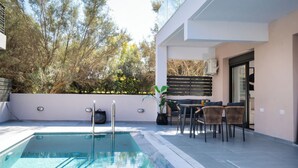 A modern outdoor pool area with a seating arrangement and a view of trees.