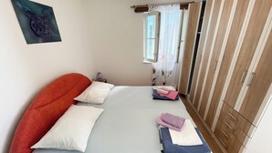 A bedroom with a bed, pillows, a bedside table, a lamp, and a window with curtains. - Apartment Fruk 1 (Jadranovo)