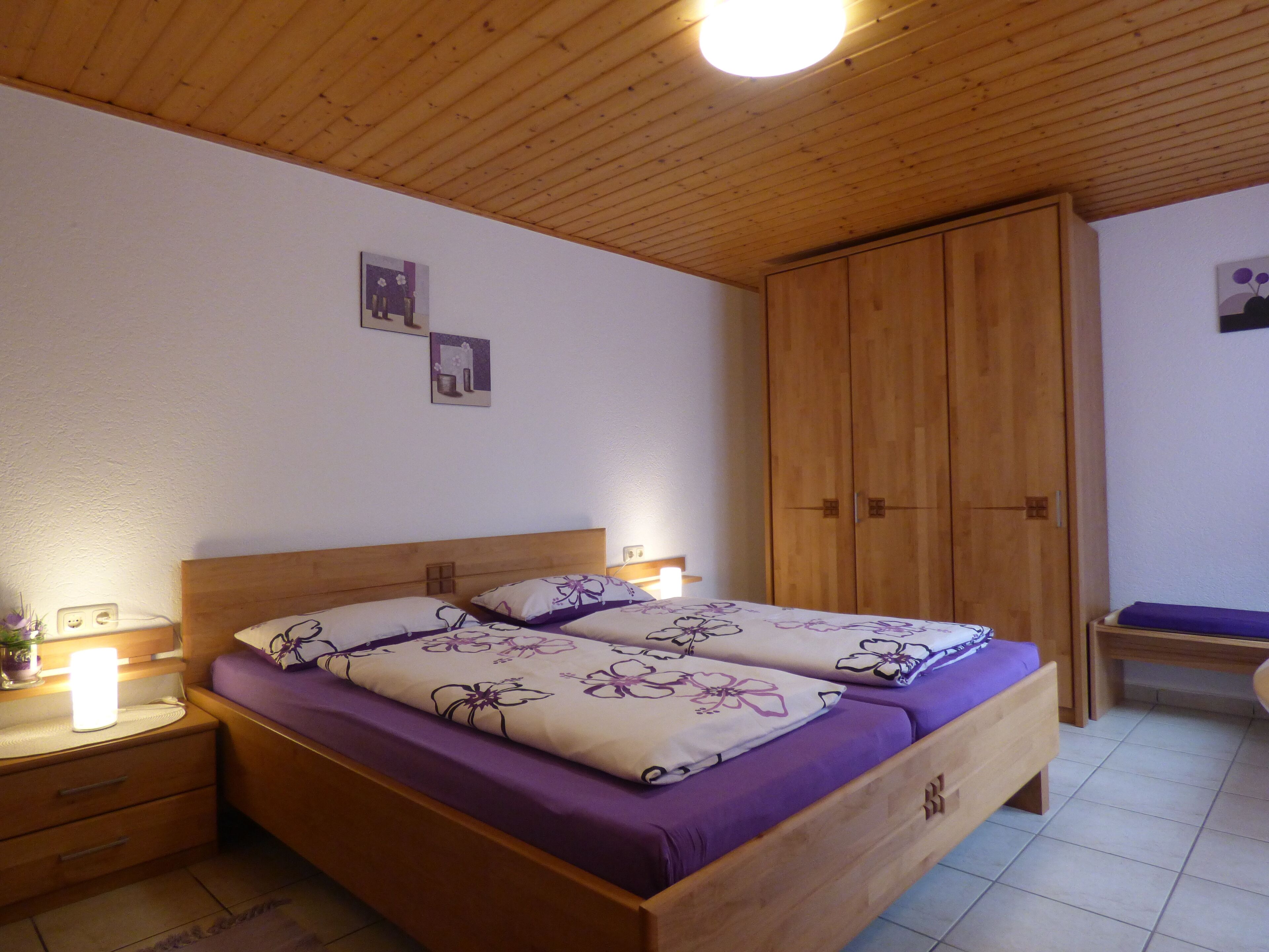 A bedroom with two wooden beds, a wooden wardrobe, and a nightstand with a lamp.