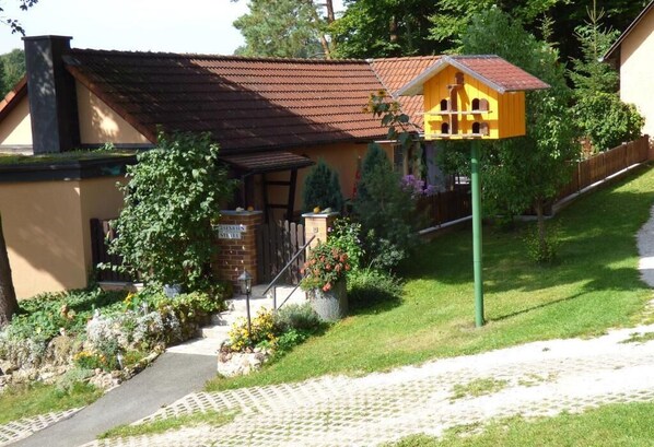 Una casa con jardín, un sendero y un comedero amarillo para pájaros.