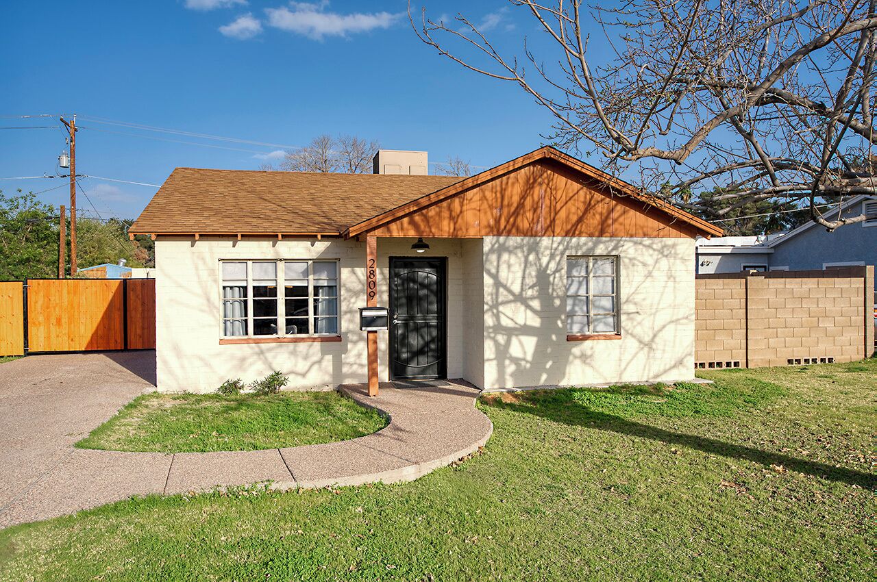 A small, single-story house with a brown roof and beige walls, a front door, and a mailbox.