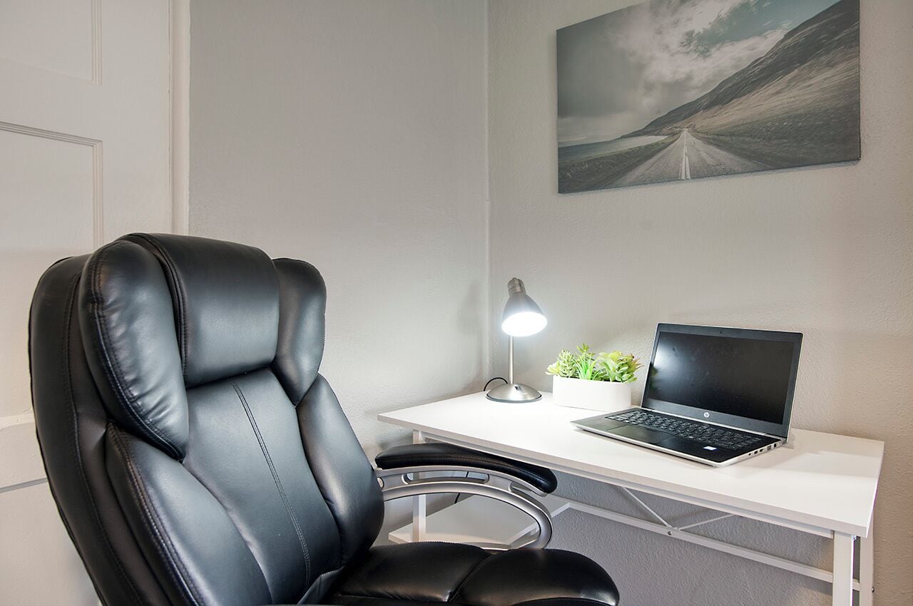 A modern office chair, a desk with a laptop, a desk lamp, and a small plant.