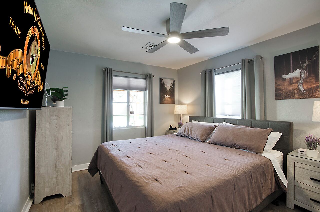 A bedroom with a bed, a ceiling fan, a nightstand, a lamp, and a window.