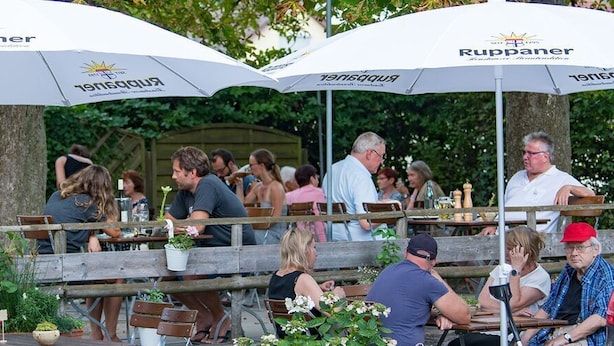 An outdoor seating area with tables and chairs under umbrellas, surrounded by greenery. - Gasthaus Adler (Konstanz)