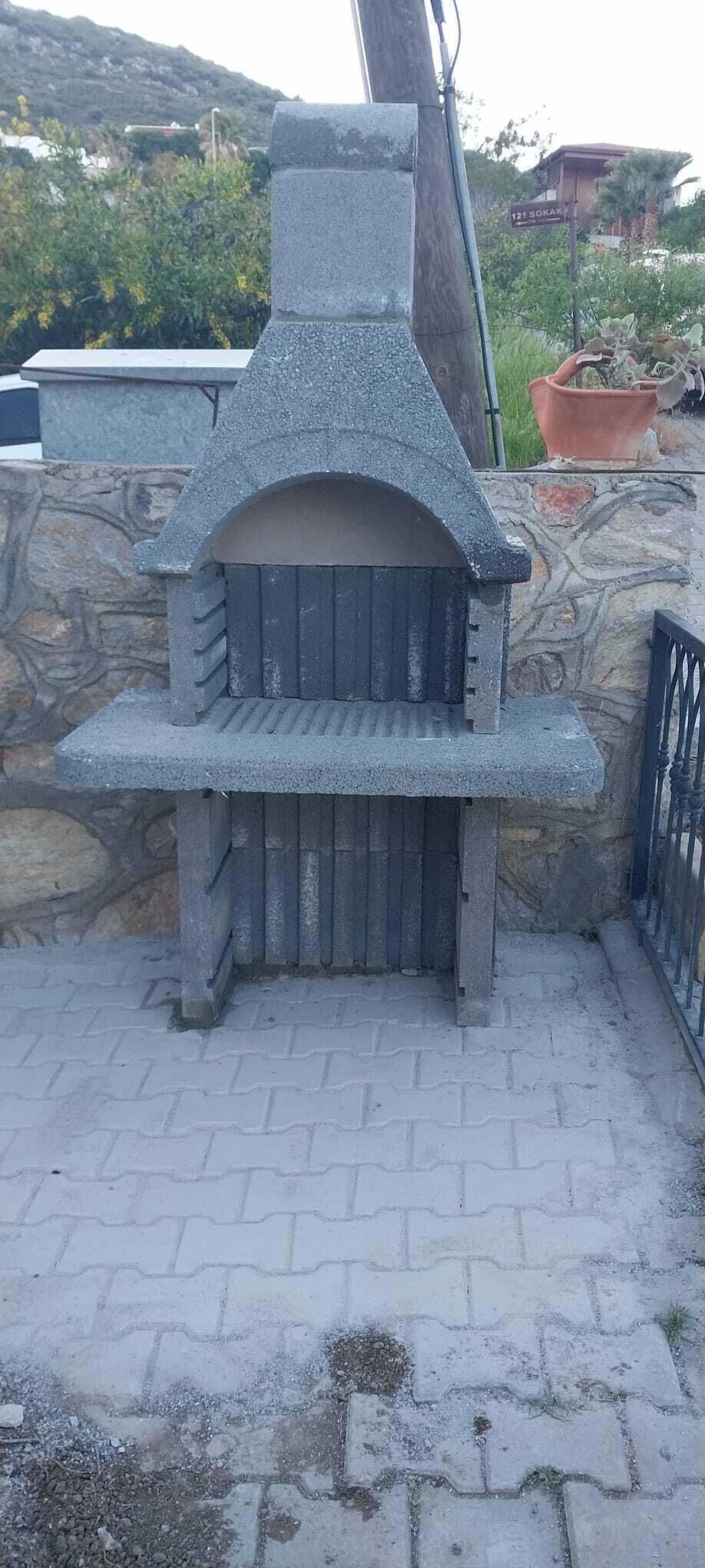 Un horno de piedra al aire libre con chimenea, frente a una pared de piedra y un área pavimentada.