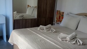 A neatly made bed with a white duvet and two towels, a wooden headboard, a mirror, and a small shelf with a decorative item. - Datça Zeytinevleri Apart (Datça)