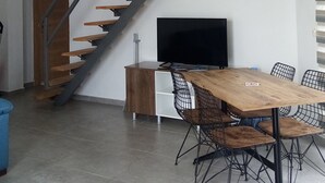 A modern interior with a wooden staircase, a dining area with a large table and chairs, and a flat-screen TV. - Datça Zeytinevleri Apart (Datça)