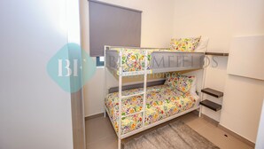 Una cama litera con ropa de cama estampada, una ventana con persiana y un pequeño estante.