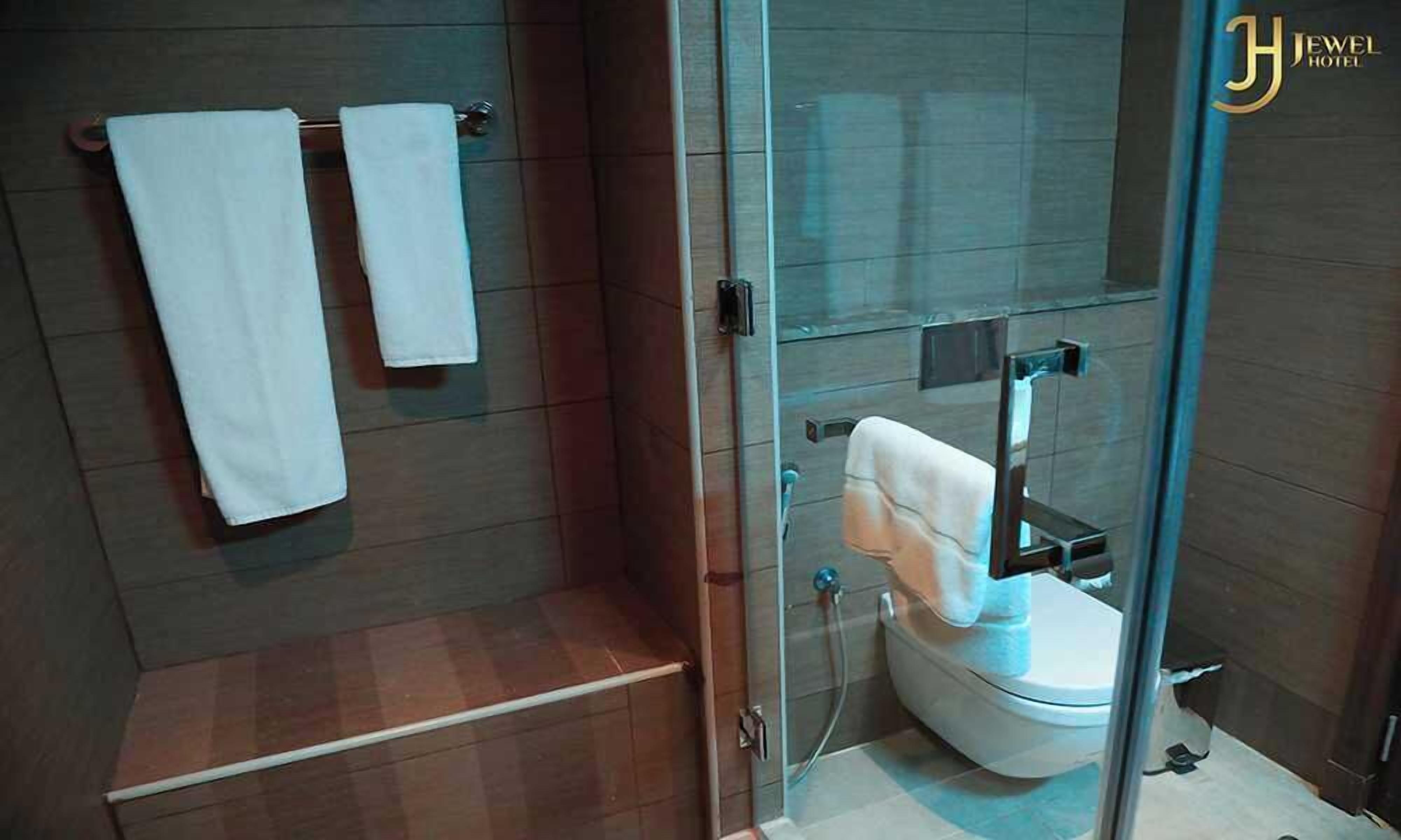 A modern bathroom with a glass-enclosed shower, a toilet, and two white towels hanging on a rack.