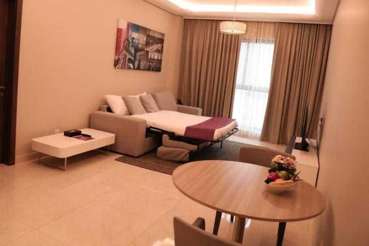 Une chambre d’hôtel moderne avec un canapé-lit, une petite table ornée d’un vase de fleurs et une grande fenêtre avec des rideaux.