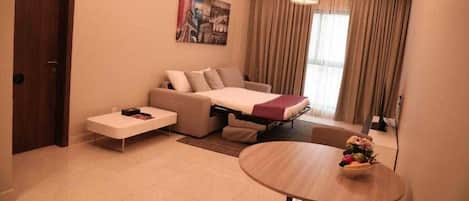 Ein modernes Hotelzimmer mit Schlafsofa, einem kleinen Tisch mit Blumenvase und einem großen Fenster mit Vorhängen.