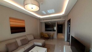 Een moderne woonkamer met een modulaire bank, een flatscreen-tv en een eethoek met gele stoelen.