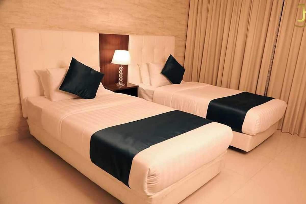 Une chambre d’hôtel avec deux lits, une table de chevet avec une lampe et une fenêtre avec des rideaux.