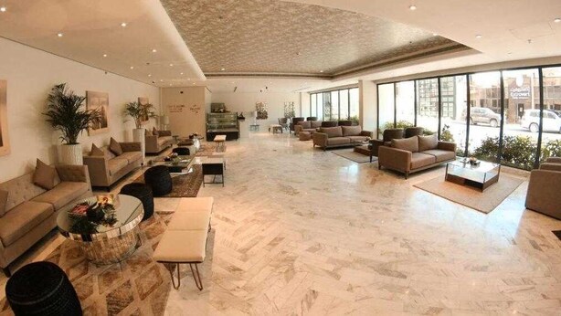 Een ruime lobby met meerdere zithoeken, grote ramen en een modern interieur.