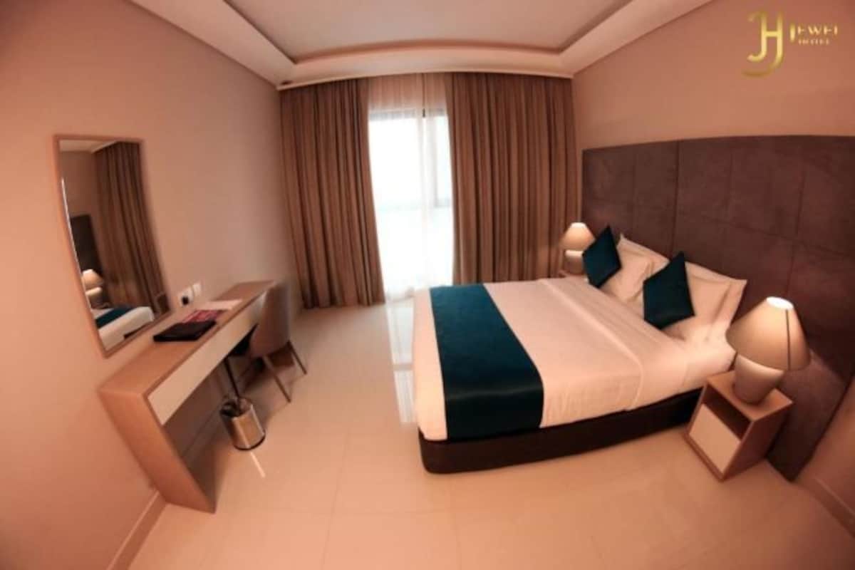 Una habitación de hotel moderna con una cama grande, mesitas de noche, un escritorio y un espejo.