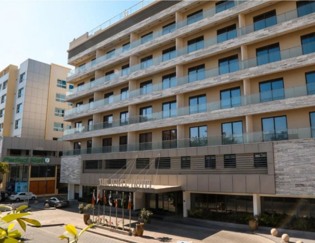 A multi-story hotel with a modern facade, a central entrance, and a parking area visible in the foreground.
