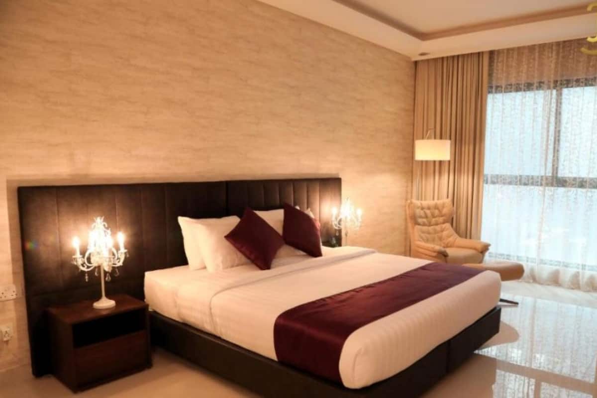 Une chambre d’hôtel avec un grand lit, une table de chevet, une chaise et une fenêtre avec des rideaux.