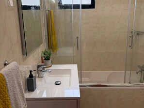 A bathroom with a glass-enclosed shower, a white sink with a mirror above it, and a bathtub.