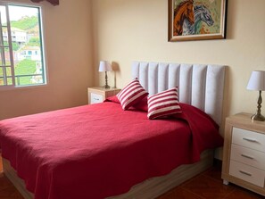 A bedroom with a bed, two nightstands, a window, and a painting on the wall.