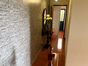 A hallway with a textured wall, a wooden floor, a mirror, and a vase with flowers.