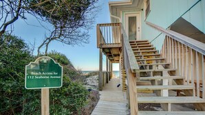 Ein hölzerner Steg führt zu einem Strandhaus mit einer Treppe.