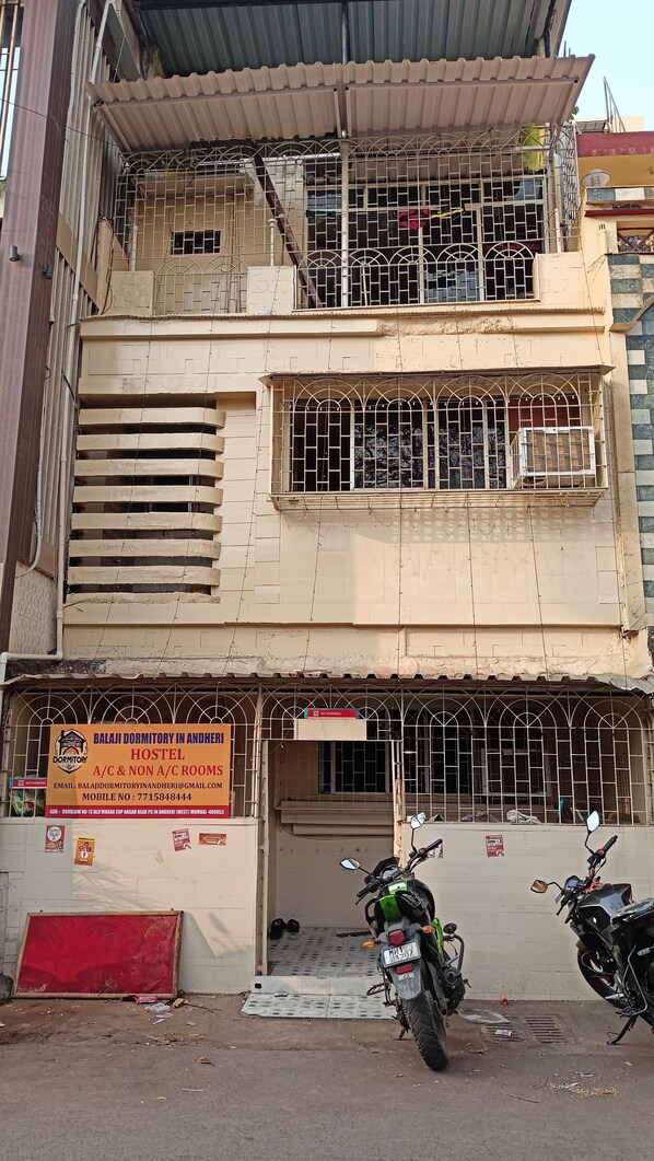 A multi-story building with a signboard advertising Balaji Dormitory in Andheri, offering A/C and non-A/C rooms.