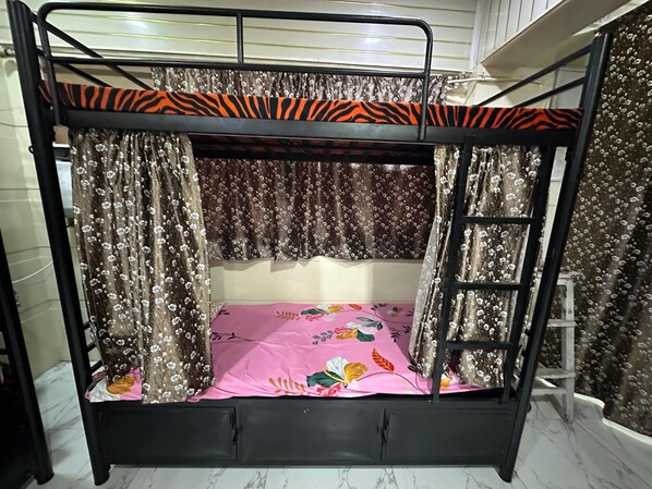 A bunk bed with a zebra-striped top rail, floral curtains, and a pink floral bedspread.