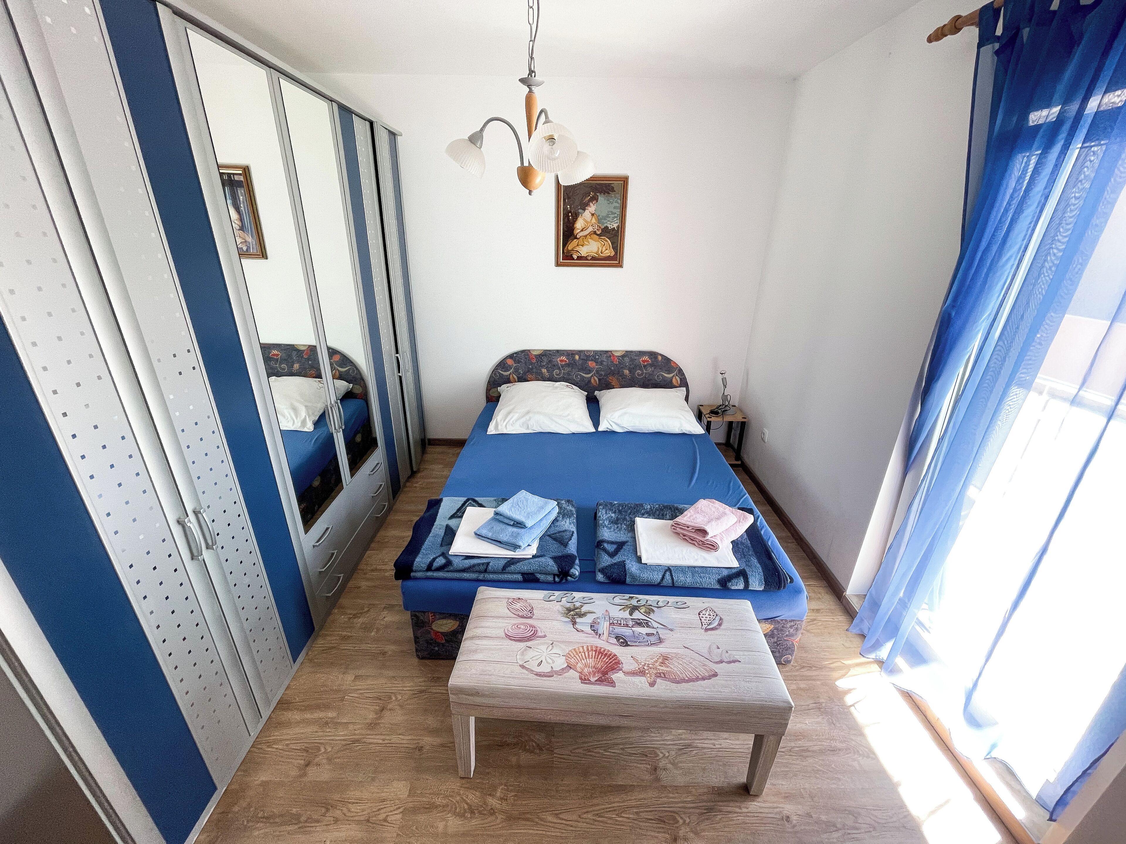 Een slaapkamer met een bed, nachtkastje, spiegel en raam met gordijnen.