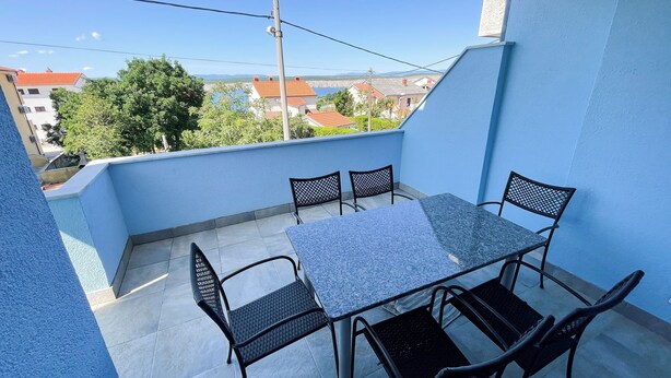 Ein Balkon mit Tisch und Stühlen, Blick auf Gebäude und Bäume, und eine blaue Wand.