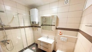 Ein Badezimmer mit Duschkabine aus Glas, einem weißen Waschbecken, einem Spiegel und einer Toilette.