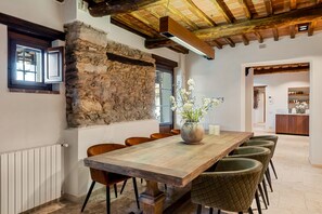 A dining area with a rustic stone wall, wooden ceiling beams, and a large wooden table with chairs.