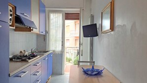 A compact kitchen with a gas stove, blue cabinets, and a dining area with a wooden table and a blue glass bowl. - Casa Romana  (Sanremo)