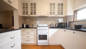 A kitchen with white cabinets, a stove, a microwave, and a toaster. - Charming older cottage in Ballarat Central with classic character, modern comfort and a great central location. Two bedrooms, full kitchen, comfy lounge, workspace and easy access to cafés, shops and attractions. (Ballarat Central)