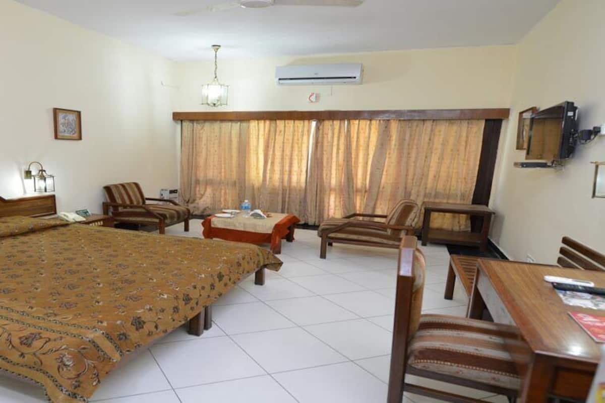 Una habitación de hotel con una cama grande, dos sillones, una mesita y un televisor.