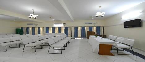 A conference room with rows of white chairs, a podium, and a flat-screen TV on the wall.