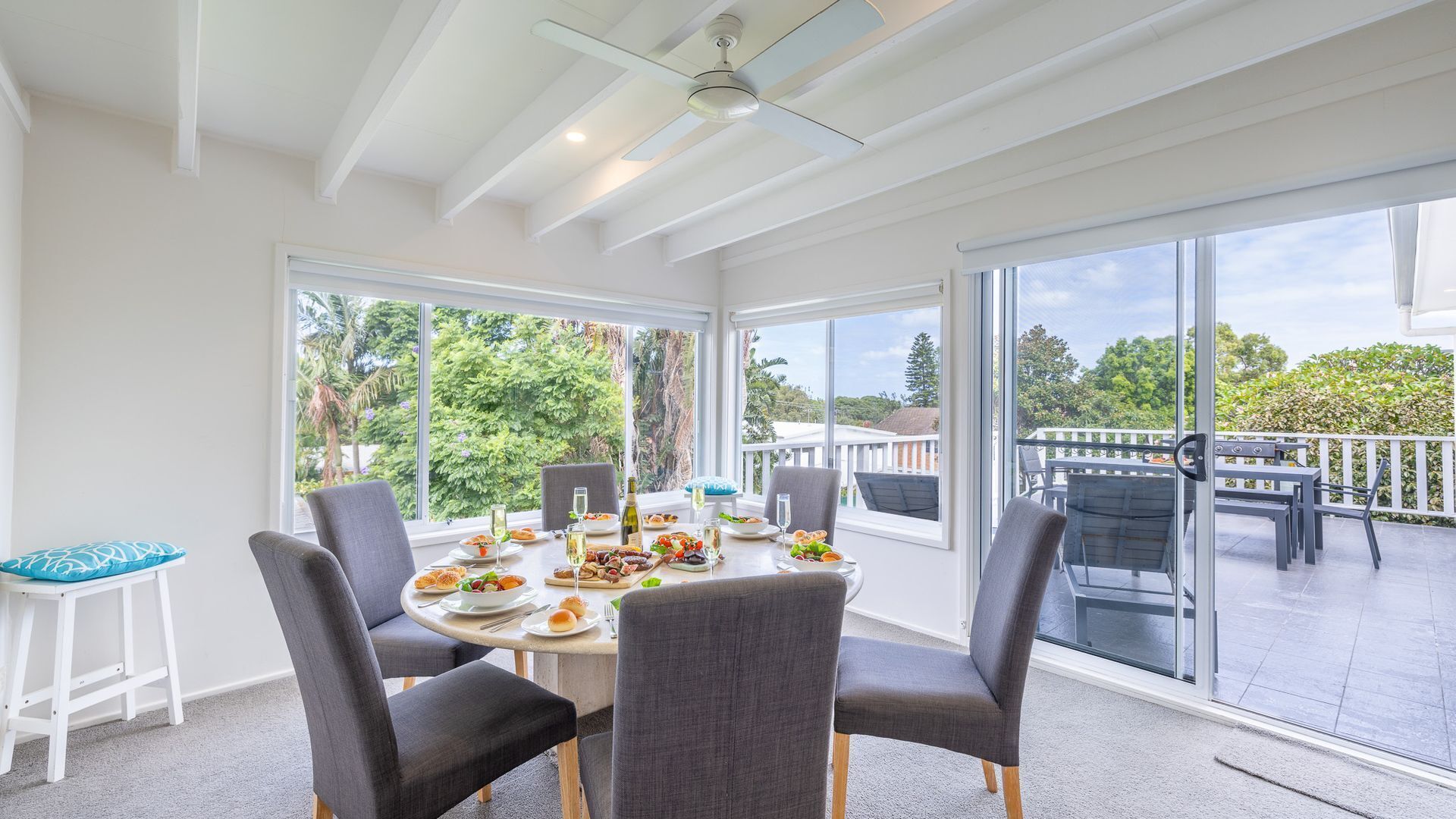A dining area with a round table, four chairs, and a view of a balcony with outdoor furniture.