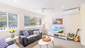 Ein Wohnzimmer mit einem schwarzen Ledersofa, einem weißen Couchtisch und einem Fernseher, der eine Küstenlandschaft zeigt.
